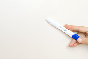 Woman hand holding a positive pregnancy test on pink background.