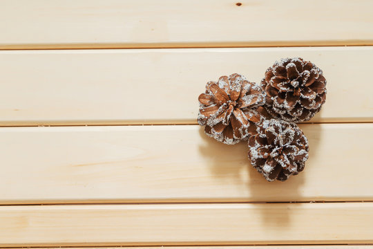 Natural fir cones covered with imitation of snow on a light wooden background. Fake artificial snow on cones on a wooden table made of planks