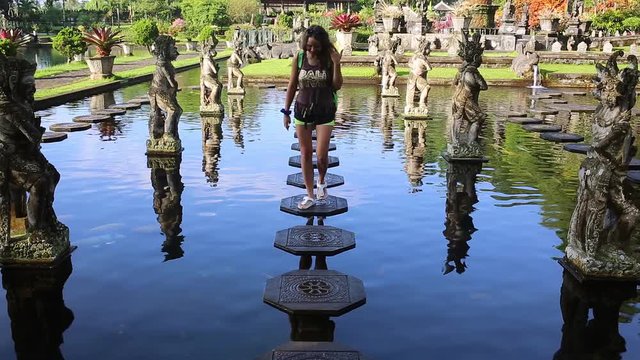 Slowmotion shot of a young woman tourist visiting the Tirta Gangga water palace, former royal palace on the Bali Island, Indonesia