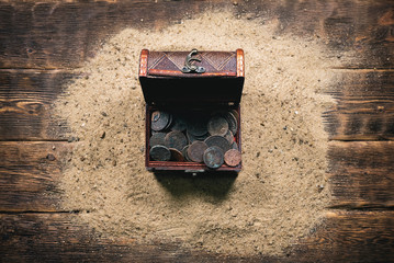 Pirate treasure chest with ancient coins on the sand on the wooden desk table background.