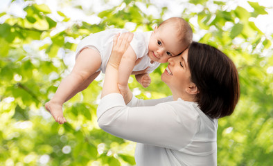 Obraz premium family, child and parenthood concept - happy smiling middle-aged mother holding little baby daughter over green natural background