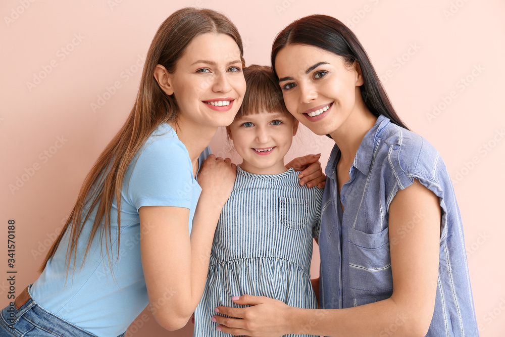 Wall mural Happy lesbian couple with little adopted girl on color background