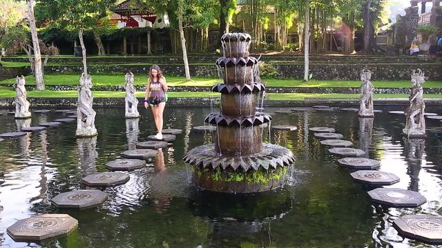 Slowmotion shot of a young woman tourist visiting the Tirta Gangga water palace, former royal palace on the Bali Island, Indonesia