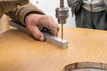A worker makes a hole in a rectangular aluminum pipe using a drilling machine