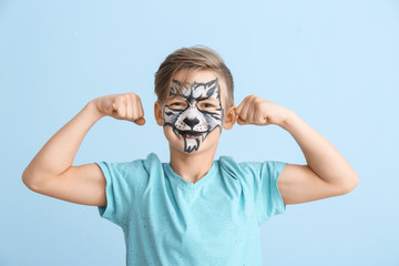 Funny little boy with face painting on color background