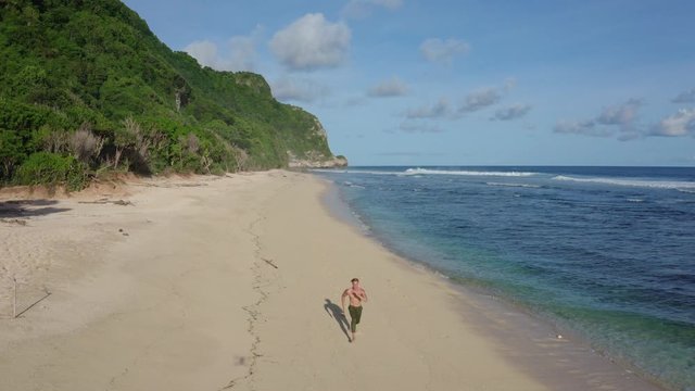 Aerial view sportsman runs alone on sandy beach, ocean, mountains on background