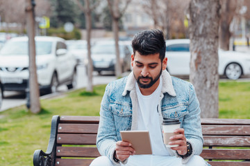 Fototapeta premium Bearded Indian man sitting on a bench and using his tablet.