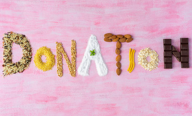 The word donation made of different type of groats, nuts, chocolate, sugar and pasta. Pink background, top view, copy space. 