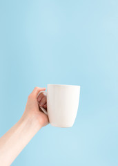 Woman holding white cup on blue background and copy space, vertical. Template mockup mug in hand