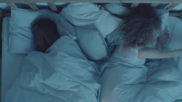 Flat lay of young diverse couple sleeping in bed. Then curly-haired woman taking her mobile phone and starting messaging