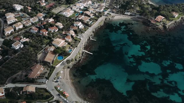 Straight down drone view of turquoise water of bay, beach, seaside promenade and white houses with tiled roofs on it, narrow streets of coastal spanish town Cadaques