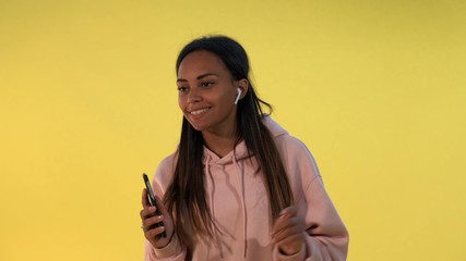 Cheerful african girl listening to the music in wireless headphones on yellow background. She is melomaniac.