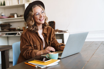 Image of cheerful woman working with laptop while sitting at table