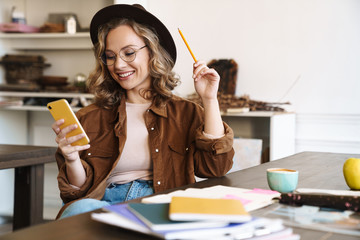 Image of woman using cellphone while studying with exercise books