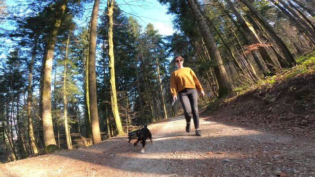 Woman in casual clothes walking with small black dog in nature, footage with action camera