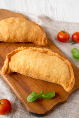 Homemade Deep Fried Italian Panzerotti Calzone on a rustic wooden board on a white wooden table, side view. Close-up.