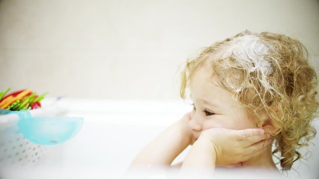 Curly blonde baby girl washes her face and hair in bathroom