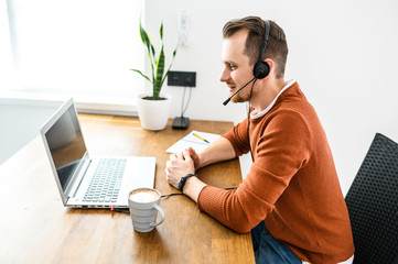The guy uses hands-free headsets to work from home. He sits at a table with a laptop and speaks...
