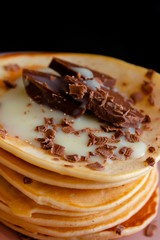 Close-up of delicious pancakes in a pink plate, with chocolate and condensed milk on a dark background.