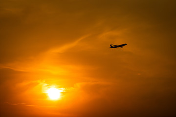 Fototapeta na wymiar Silhouette photo of Airplane flight during flying in dramatic orange sky and burning sun as background. Travel destination and transportation activity concept.