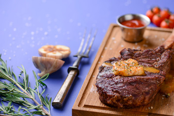 Grilled Medium rare barbecue Steak on bone with spices served on a rustic wooden board with sauce over blue background.