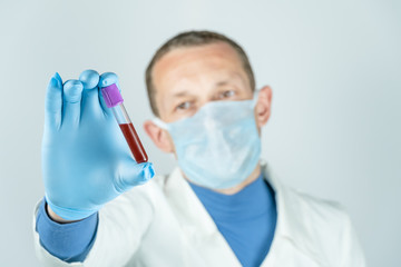 Male doctor in a medical gown, mask and gloves holds a test tube with blood. Concept of medical...