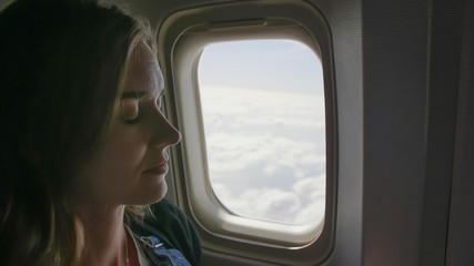 A young woman is sleeping at the window of an airplane.