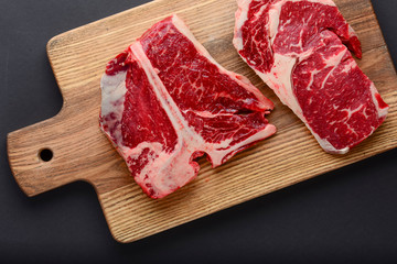 Fresh raw beef steak on wooden cutting board, top view. Served over black background.