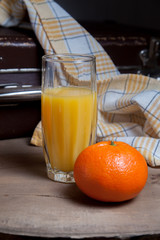 Unpeeled round ripe orange mandarins or tangerines and glass of fresh juice on wooden board.