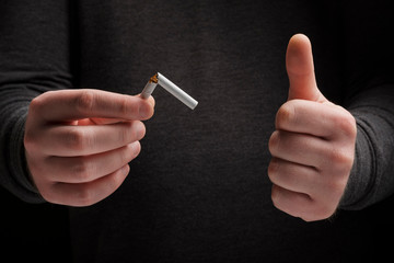 Male holding a broken cigarette and showing thumbs up. Stop smoking cigarettes concept. Quit bad habit, healthy lifestyle concept. No smoking. Do not choose wrong lifestyle.