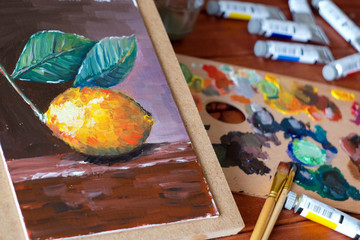 Close up oil painting process. Oil paints palette. Oil painting tools on the wooden table. Painter work place. Lemon oil painting on the canvas.