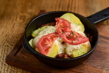Meat and mushroom gratin with cheese and tomatoes served in a pan over dark wooden table background. Ukrainian cuisine.