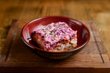 Traditional Russian herring salad served in a bowl on dark wooden table background in a restaurant.