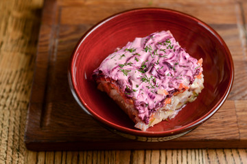 Traditional Russian herring salad served in a bowl on dark wooden table background in a restaurant.