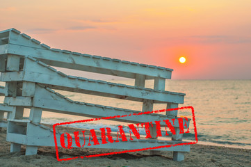 Obraz premium Folded wooden deck chairs on a deserted beach by the sea. Quarantine on summer sea vacation. The failure of the sea season. Coronavirus COVID-19. Red stamp seal QUARANTINE. Closed city public beaches