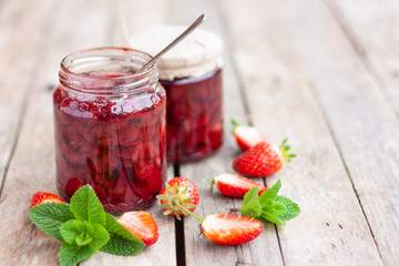 Srawberry jam in a glass jar with some fresh strawberry on wooden old rustic table. Homemade strawberry marmelade and fruits. Selective focus. Top view