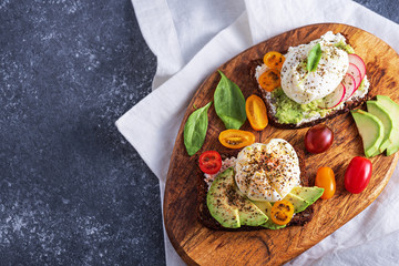 vegetarian toast with poached eggs, cottage cheese, avocado, spinach, cherry tomatoes on wooden Board on gray background