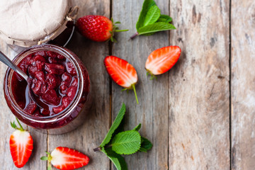 Srawberry jam in a glass jar with some fresh strawberry on wooden old rustic table. Homemade strawberry marmelade and fruits. Selective focus. Top view