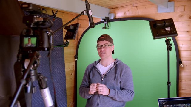 Energetic presentation by male wearing casual clothes, cap and glasses in front of green screen.