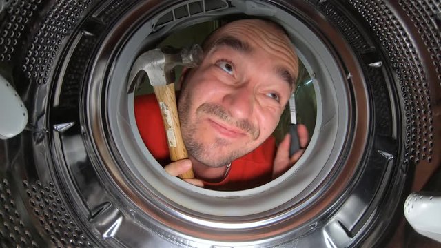 A Man Holding Hammer And Screw Driver Looking What To Fix Inside The Washing Machine - Closeup Shot