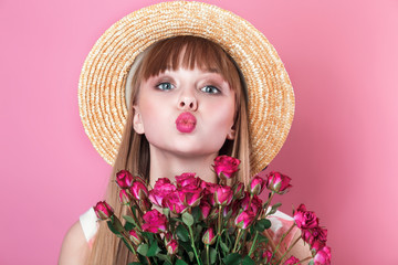 Woman with flowers sends air kiss on pink background