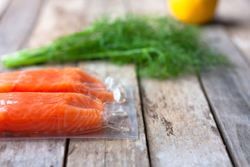 Red fish o salmon fillets in vacuum package on wooden background. Fresh fish, lemon and dill for cooking ingredients. Concept of healthy eating. Omega-3. Selective focus. Close up. Copy space