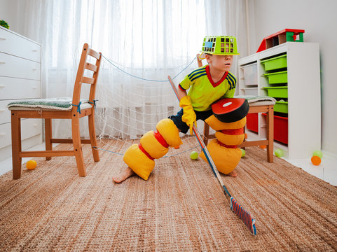 A child boy plays hockey at home having made a form with his own hands from improvised home tools and a gate made of chairs.