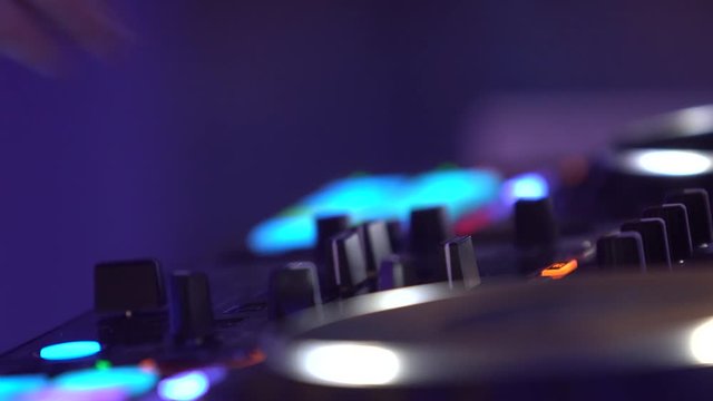 Closeup of a deejay mixing music on a console at the night club party. DJ plays on the famous CD players at a nightclub. DJ Spinning, Mixing, and Scratching. Various track controls on dj's deck.