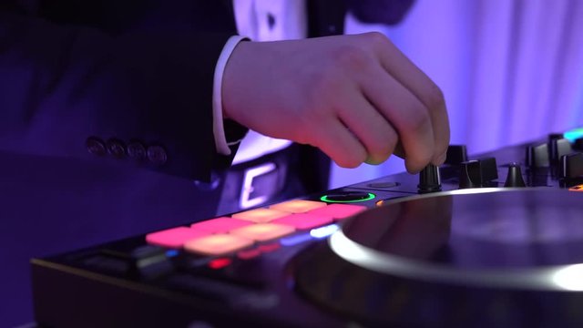 DJ in a formal dress mixing music on a console at the night club party. DJ plays on the famous CD players at a nightclub. DJ Spinning, Mixing, and Scratching. Various track controls on dj's deck.