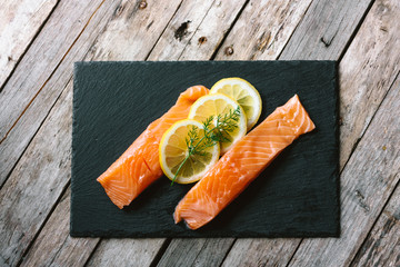 Red fish o salmon fillets on stone slate on wooden background. Fresh fish, lemon and dill for...