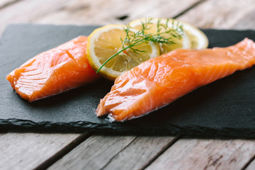 Red fish o salmon fillets on stone slate on wooden background. Fresh fish, lemon and dill for cooking ingredients. Concept of healthy eating. Omega-3. Close up.