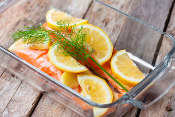 Red fish o salmon fillets in.glass baking dish on wooden background. Fresh fish, lemon and dill for cooking ingredients. Concept of healthy eating. Omega-3. Close up.