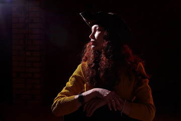 Portrait of elegant woman with long hair hat and in yellow sweater and dark background. Model posing doring studio photo shot