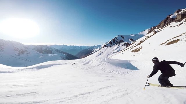 slow motion view of a skier dressed in black gracefully skiing in the mountains with beautiful sunlight rays shining with the beautiful mountain backdrop in the french alps ski resort